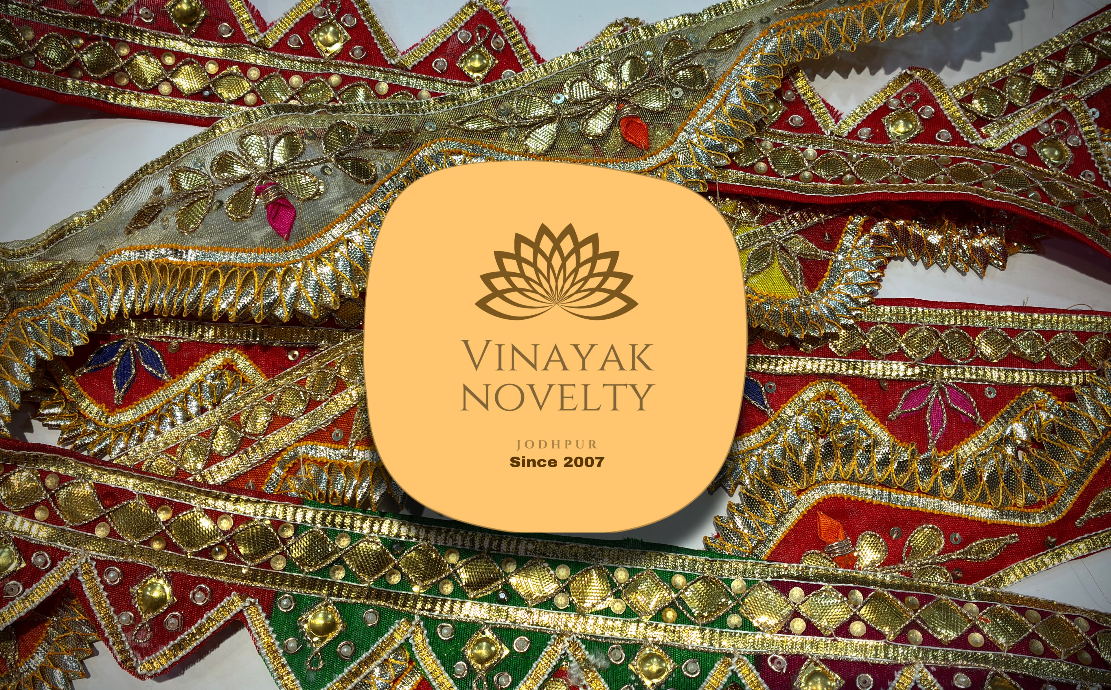 Decorative fabric with gold and red patterns featuring the Vinayak Novelty logo.